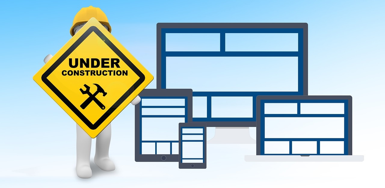 An illustration of a worker holding an “under construction” sign next to electronic devices, highlighting the importance of website maintenance.