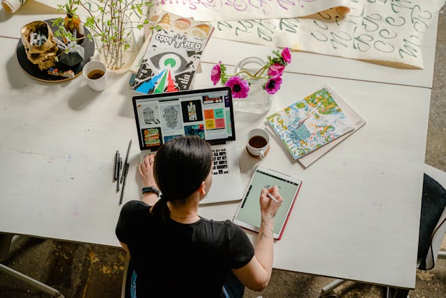 A woman writing on a tablet while using her laptop